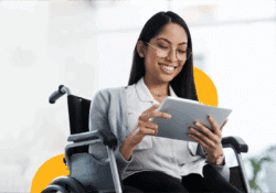 A smiling woman in a wheelchair uses a digital tablet in a bright, modern workspace. She is wearing glasses and business attire, symbolizing digital inclusion and professional accessibility.